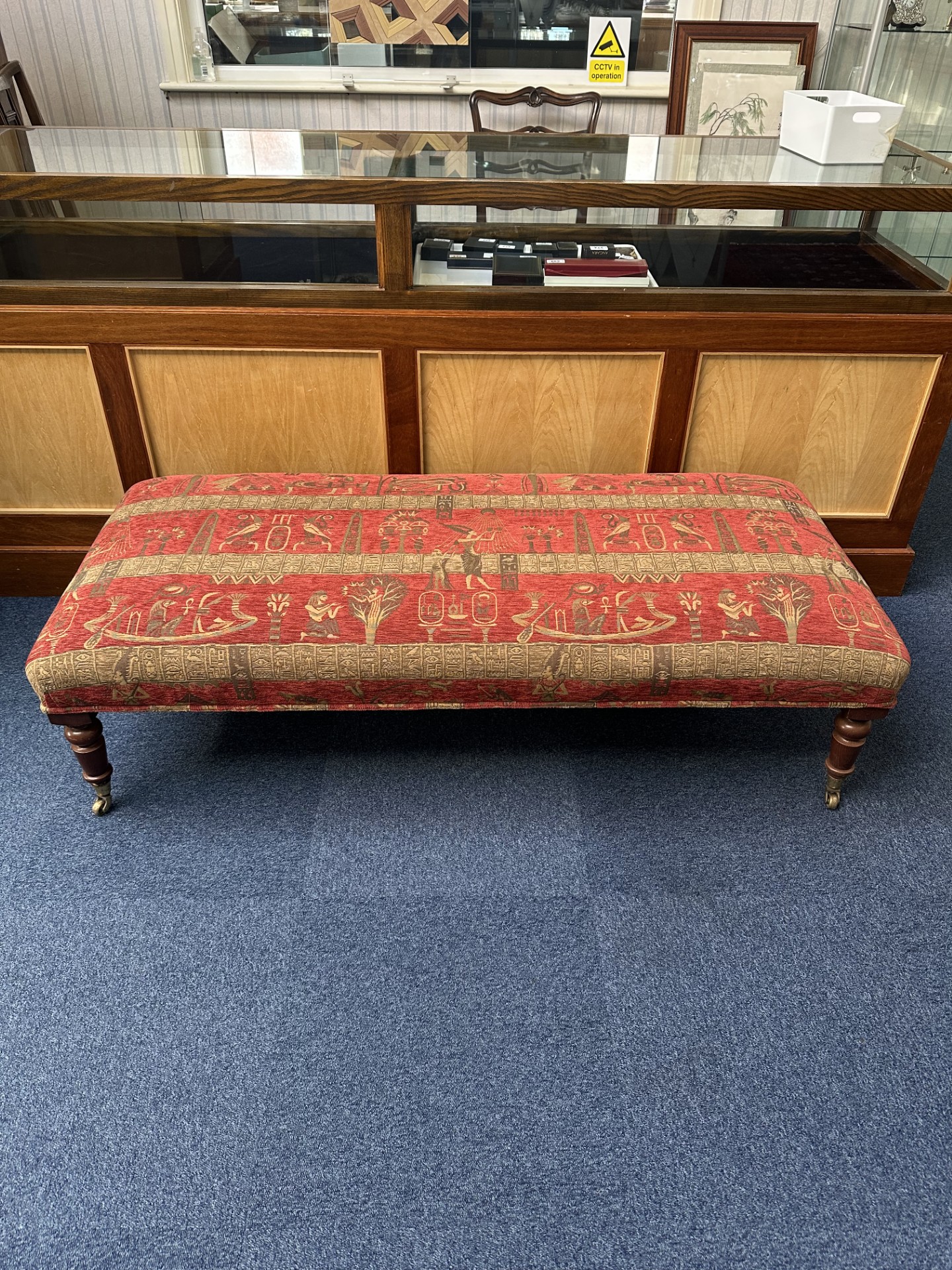 Low Upholstered Bench raised on legs with castors. Covered in tapestry fabric. Measures 16'' high,