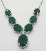 A silver necklace having central articulated panel of six graduated oval cut green stones with