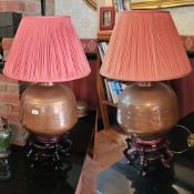 A fine pair of spherical beaten copper lamp bases, each with red pleated shade, each upon