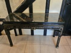 A black lacquered console table having Oriental decoration throughout, raised over carved