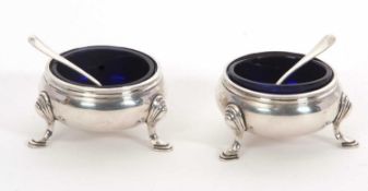 A pair of George V silver cauldron salts with blue glass liners, supported on three hoof feet,