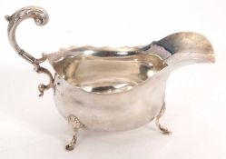 A George V silver sauce boat of typical form with flying leaf capped scroll handle, wavy rim and