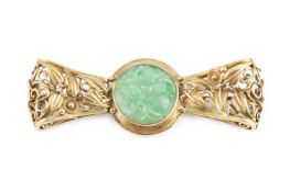 A jade panel brooch, the circular carved jadeite panel in collet setting, to a bow-shaped openwork