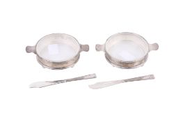 A pair of glass and silver butter dishes and a pair of butter knives.