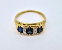 A three stone sapphire ring set with four diamonds (one sapphire stronger in colour), set in 18ct