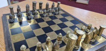 A complete brass chess set with stylised pieces, on a polished brass board.