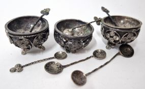 A set of three continental white metal salts, with embossed coin decoration, together with spoons.