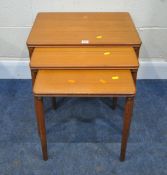 A MID CENTURY TEAK NEST OF THREE TABLES, raised on cylindrical tapered legs, largest table width