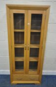 A MODERN OAK BOOKCASE, with double glass doors, over a single drawer, width 79cm x depth 36cm x
