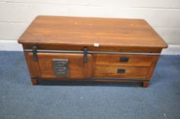 AN INDUSTRIAL STYLE MANGO WOOD DOUBLE SIDED COFFEE TABLE, with a rolling track door and two drawers,