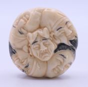 A bone netsuke formed as faces. 4 cm diameter.