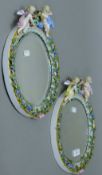 A pair of Continental porcelain mirrors, each surmounted with cherubs. Each 33 cm high.
