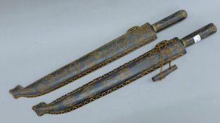 Two tribal swords in carved wooden scabbards. Each 65 cm long.