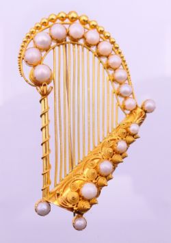 A boxed unmarked gold (14 K gold or higher) pearl set brooch formed as a harp,