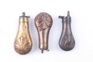 Three copper and brass pistol powder flasks, two with embossed shell decoration, the third with