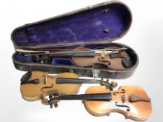 Three 20th century violins, one in coffin case with two bows.