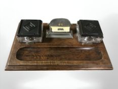 An Art Deco oak desk stand with brass inkwells and central calendar,