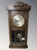 An early 20th century oak eight day wall clock with silvered dial, pendulum and key,