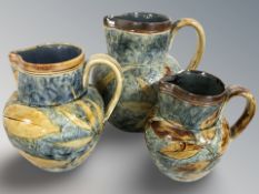 Three Royal Doulton graduated stoneware jugs decorated with leaves, tallest 19 cm.