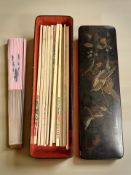 A Japanese lacquered rectangular lidded box containing assorted chopsticks and a modern hand fan.