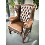 A Chesterfield style deep buttoned brown leather wing back armchair,