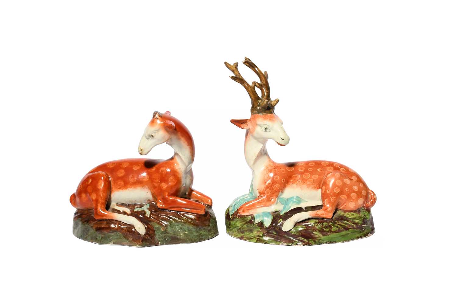 A pair of Staffordshire figures of a stag and doe, c.1810, each recumbent with head turned, raised