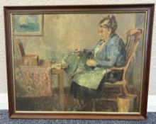 A framed oil on board depicting a woman seated at a table sewing.