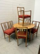 A pine drop leaf circular dining table and six chairs, upholstered in red (H74cm Dia115cm)