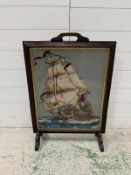 A vintage glass fronted fire screen with a central tapestry of a square rigged naval ship