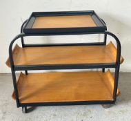 A Modernist trolley, ebonised and bent plywood three trays on industrial style wheels, with an Art