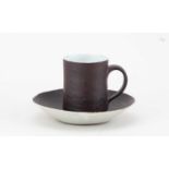 † LUCIE RIE (1902-1995); a stoneware cup and saucer covered in manganese and white glaze,