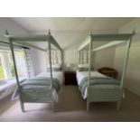 A pair of green painted four poster single beds, with turned columns and panelled base boards, on