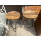 A PAIR OF BAR STOOLS WITH SOLD WOOD SADDLE SEATS ON TUBULAR METAL BLACK LEGS