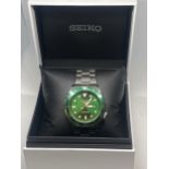 A SEIKO 5 SPORTS AUTOMATIC WRISTWATCH WITH GREEN DIAL, MATCHING BEZEL AND STAINLESS STEEL STRAP IN A