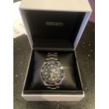A SEIKO 5 SPORTS WRISTWATCH WITH BALCK FACE, BLACK BEZEL AND STAINLESS STEEL STRAP IN A PRESENTATION