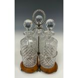 An Edwardian oak and silver plated three bottle stand, with glass decanters, beaded looping