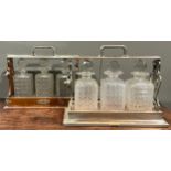 An Edwardian E.P.N.S mounted oak three bottle tantalus, hobnail-cut glass decanters with prismatic
