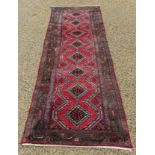 A Persian runner, with geometric motifs, on a red ground, 288 x 81.5 cm