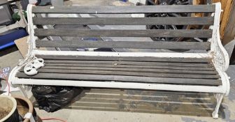 White painted metal garden bench on scrolling supports interspersed with leaves and flowers, with