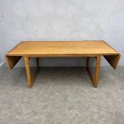 A mid-century oak extending dining table with two drop leaves raised on tapering trestle supports in