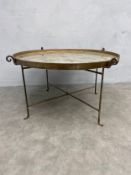 A vintage folding coffee table with circular composite resin tray top raised on scrolling x-