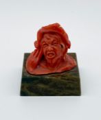A miniature Expressionist style carved coral portrait bust of a man in a hat raised on a green