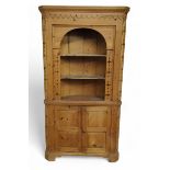 A pine floor-standing corner cabinet, moulded cornice with raised swags, pierced borders and splays,