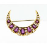 An ruby and diamond 18ct gold crescent brooch, comprising a row of oval mixed cut rubies with