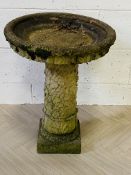 A weathered bird bath raised upon a decorative column