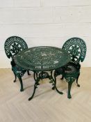 A green painted circular cast aluminium patio table and two chairs,