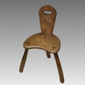 A 20th century short backed three legged milking stool, the arched back with hand hole, height 71cm,