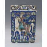 A Persian relief moulded tile, modelled and painted with a falconer on horseback with attendant,