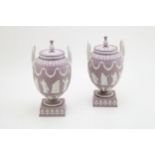 An impressive pair of Wedgwood lilac jasperware twin handled pedestal urns and covers, decorated