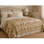 A large quilted bedspread or throw featuring a traditional botanical style print on a cream